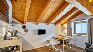 Et moderne køkken med træbjælker, et spiseområde med bord og stole, og en sofa.
