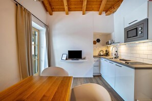 A compact kitchen with a wooden table, white cabinets, a microwave, and a window with curtains.