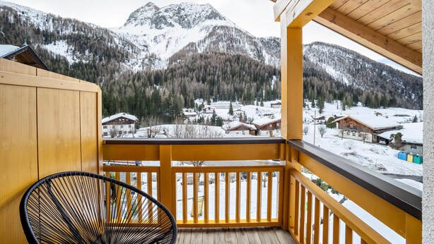 A wooden balcony with a view of snow-covered mountains and houses. - Apartment "Mountain Residence Kasern Nr 4" with Mountain View, Balcony & Wi-Fi (Prettau)