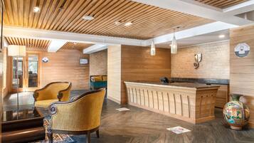 A reception area with a wooden reception desk, two upholstered chairs, a vase, and a wooden ceiling with recessed lighting.
