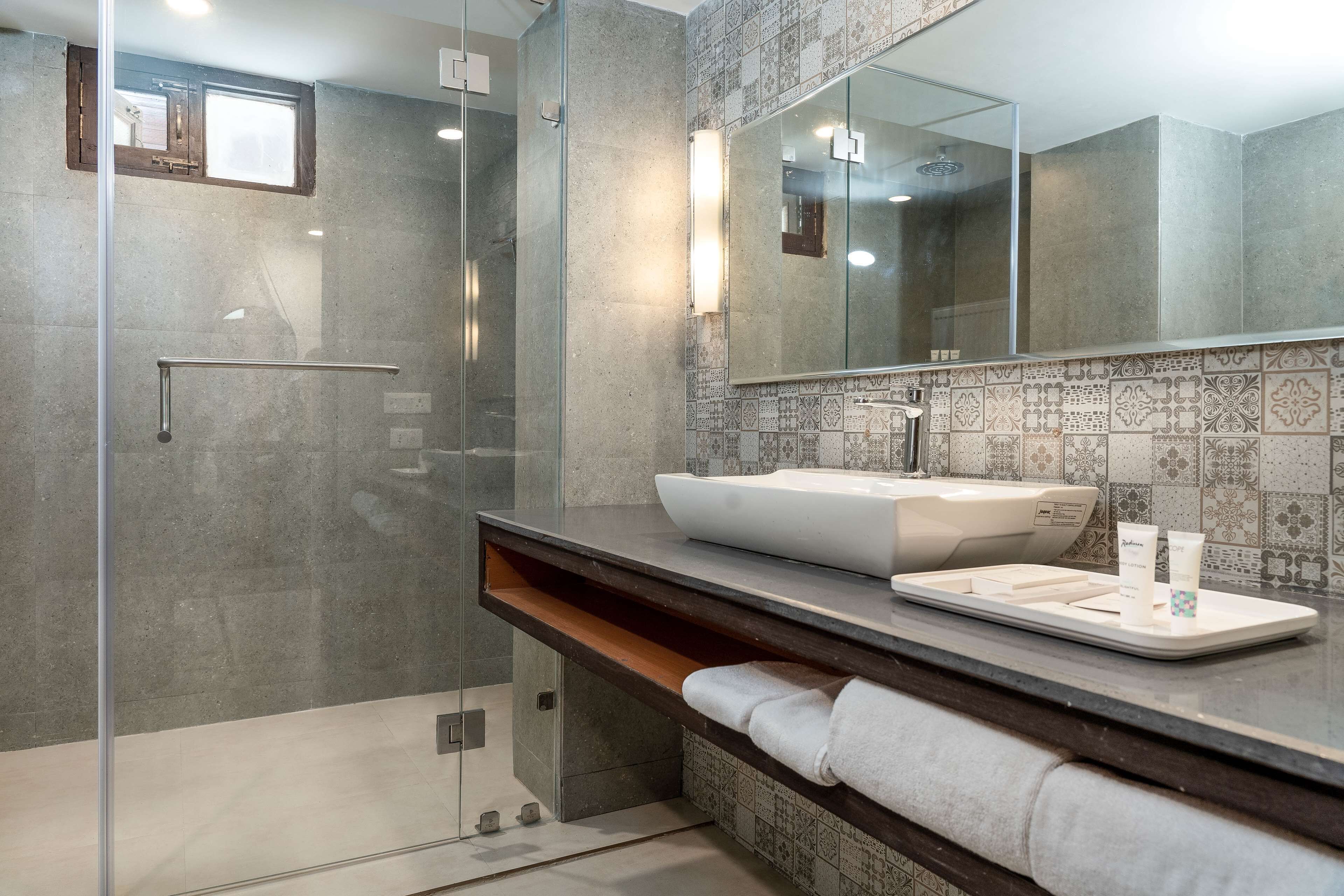 Un baño moderno con cabina de ducha de vidrio, un espejo grande y un lavamanos blanco con un recipiente.