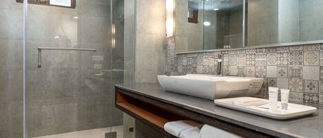 Un baño moderno con cabina de ducha de vidrio, un espejo grande y un lavamanos blanco con un recipiente.