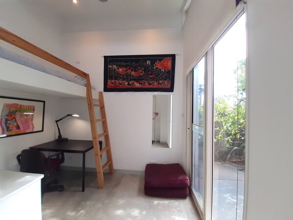 A room with a bunk bed, a desk, a chair, a ladder, a large window, and a framed picture on the wall.
