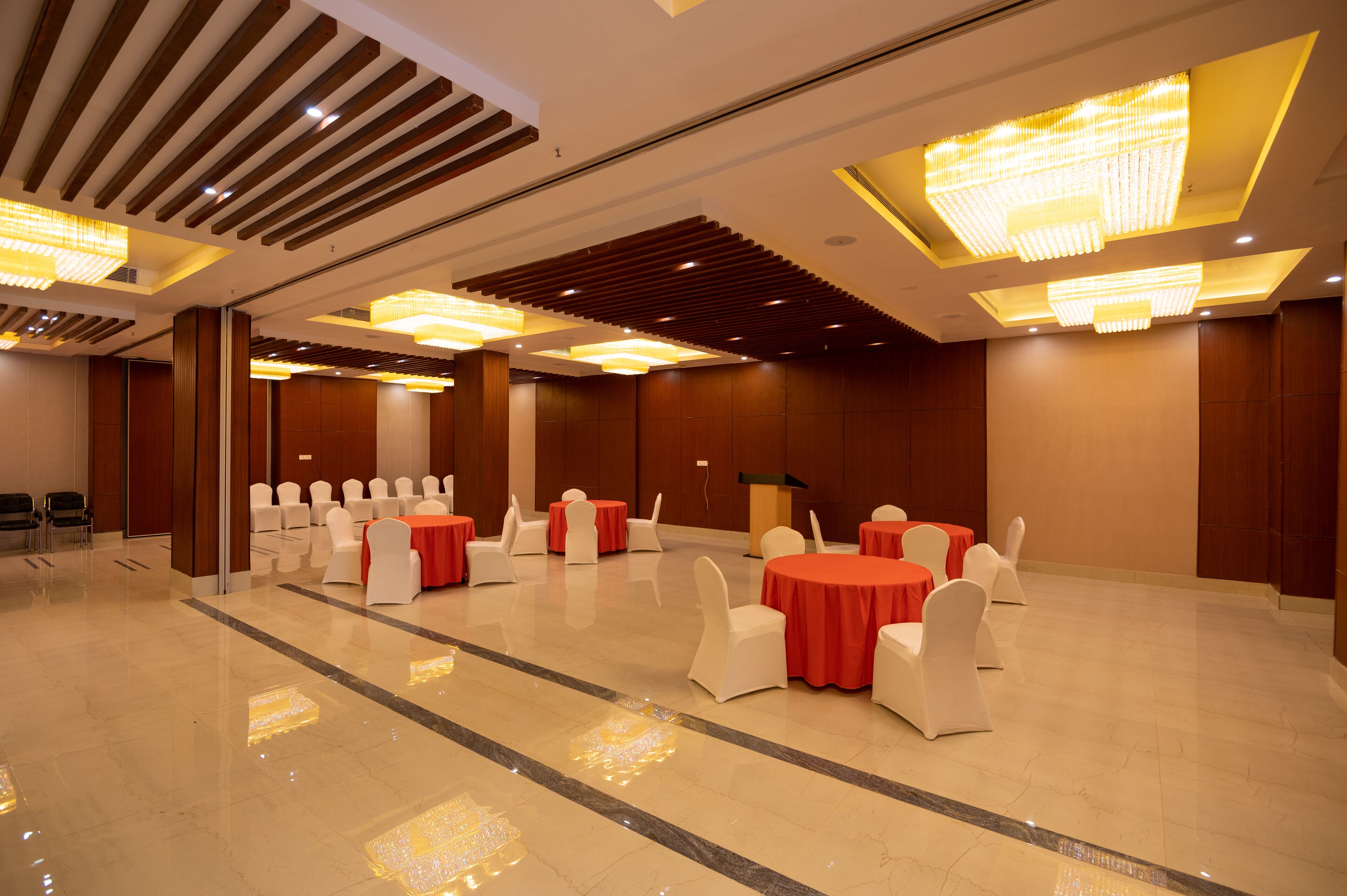 Un amplio salón de banquetes con varias mesas redondas, sillas blancas y manteles rojos.