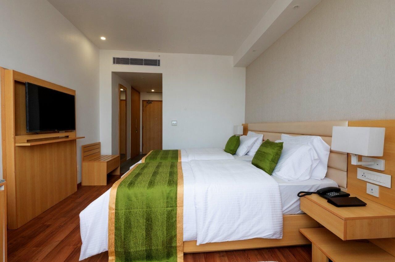 Een hotelkamer met een bed, nachtkastje, televisie en een houten bankje.