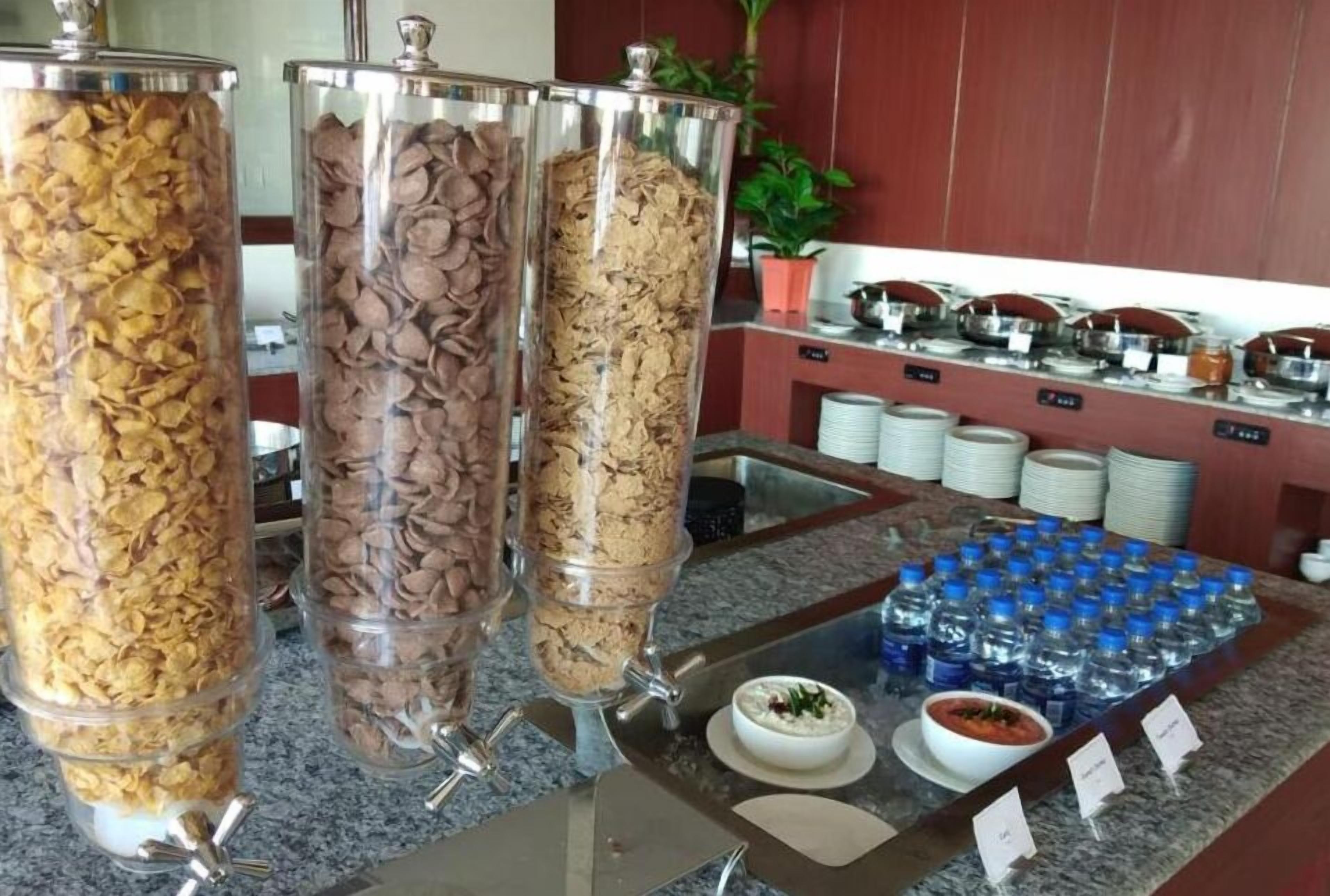 Un espace buffet proposant divers plats présentés dans des récipients transparents, un plateau de bouteilles d’eau et un petit bol de soupe.