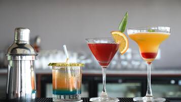 Drei Cocktails auf einer Bar, zusammen mit einem Shaker und einem Glas mit Limettenscheibe.