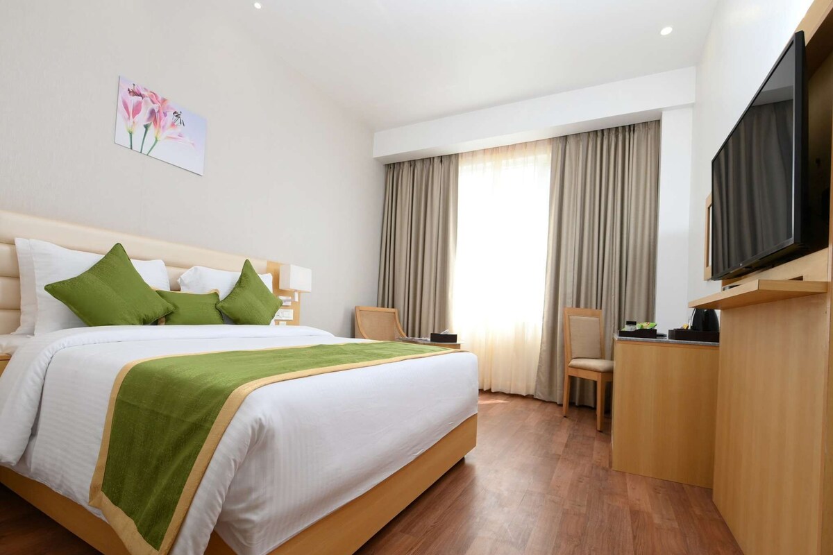 Una habitación de lujo con una cama grande, almohadas verdes, un televisor de pantalla plana, un escritorio y una silla.