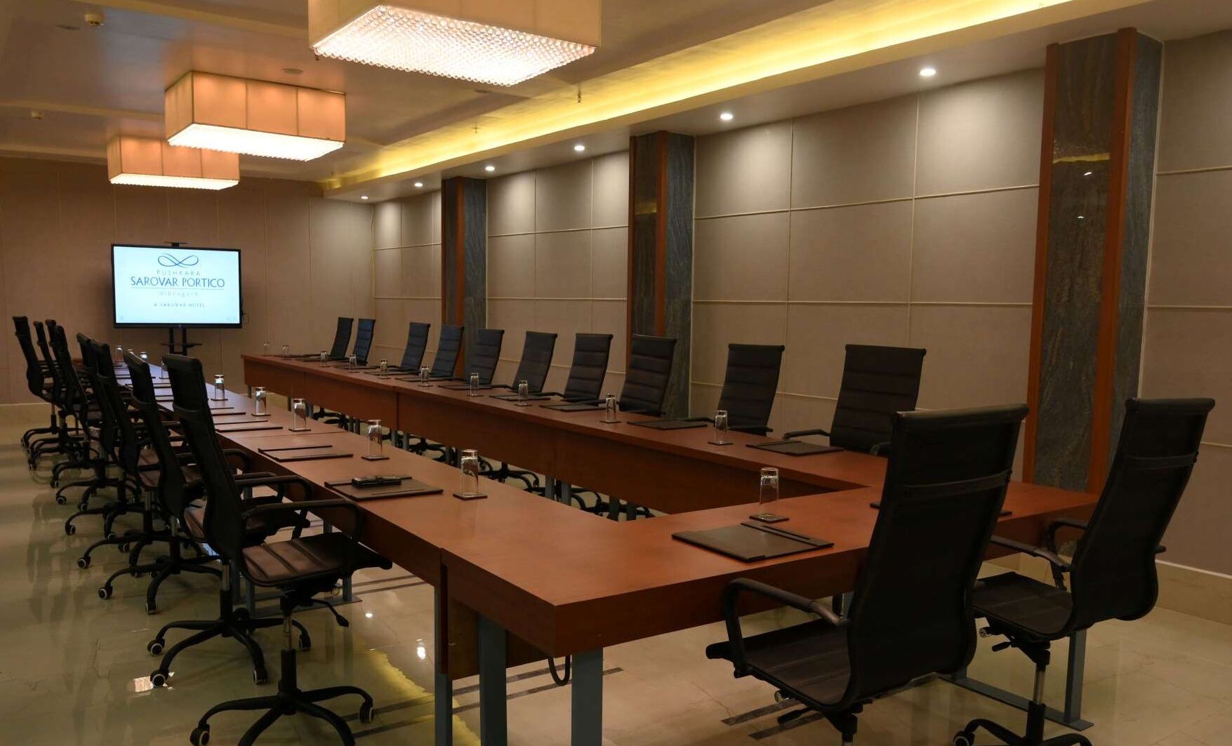 Een vergaderruimte met een lange tafel, meerdere stoelen, een scherm voor een presentatie en een presentatie aan de muur.