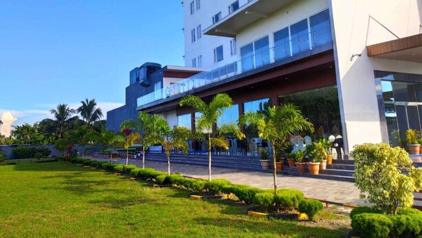 A modern hotel with a flat roof, multiple balconies, and a well-maintained garden with various plants.
