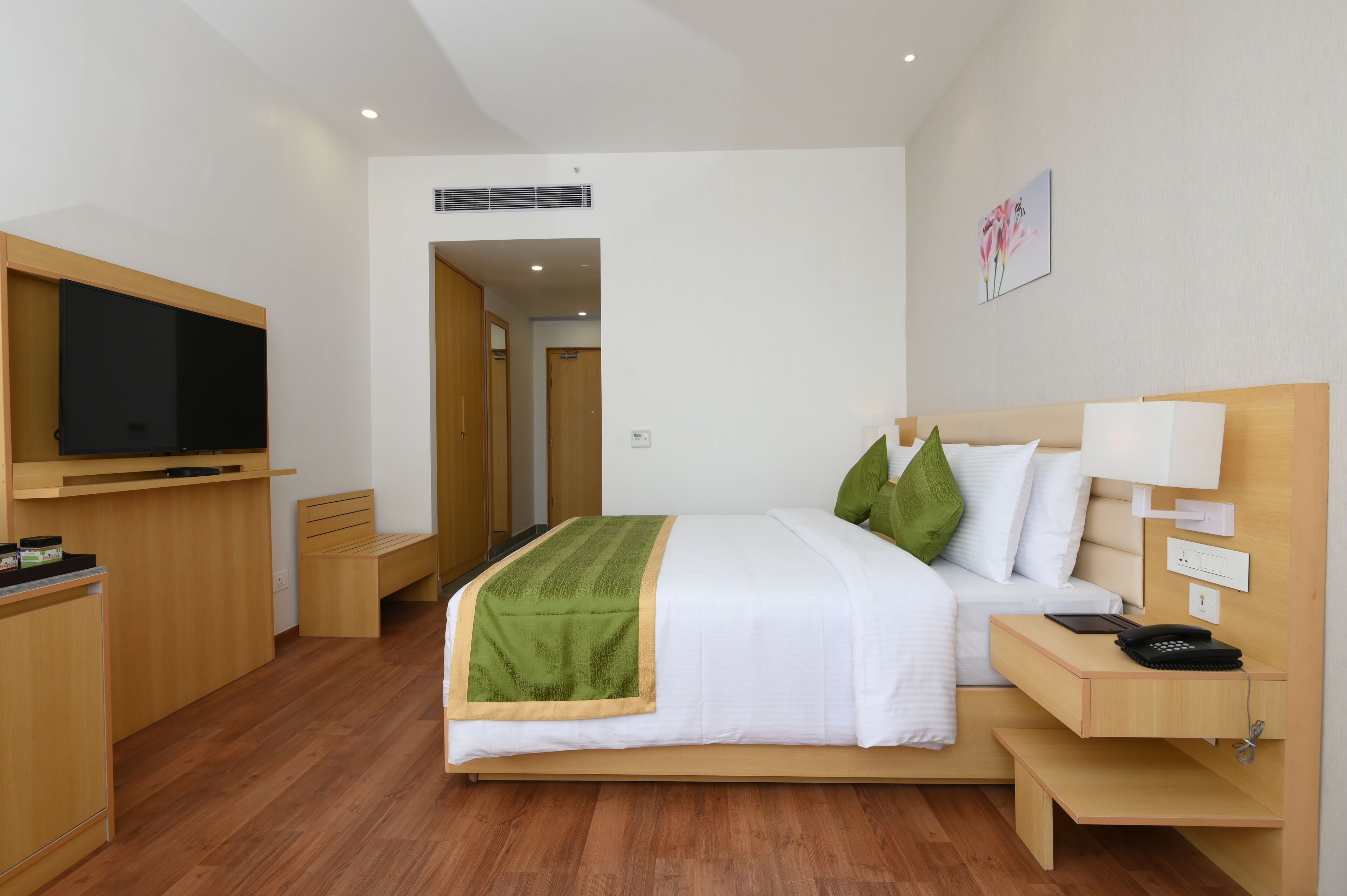 Une chambre d’hôtel moderne avec un lit en bois, une table de chevet avec une lampe, un téléviseur fixé au mur et un banc.