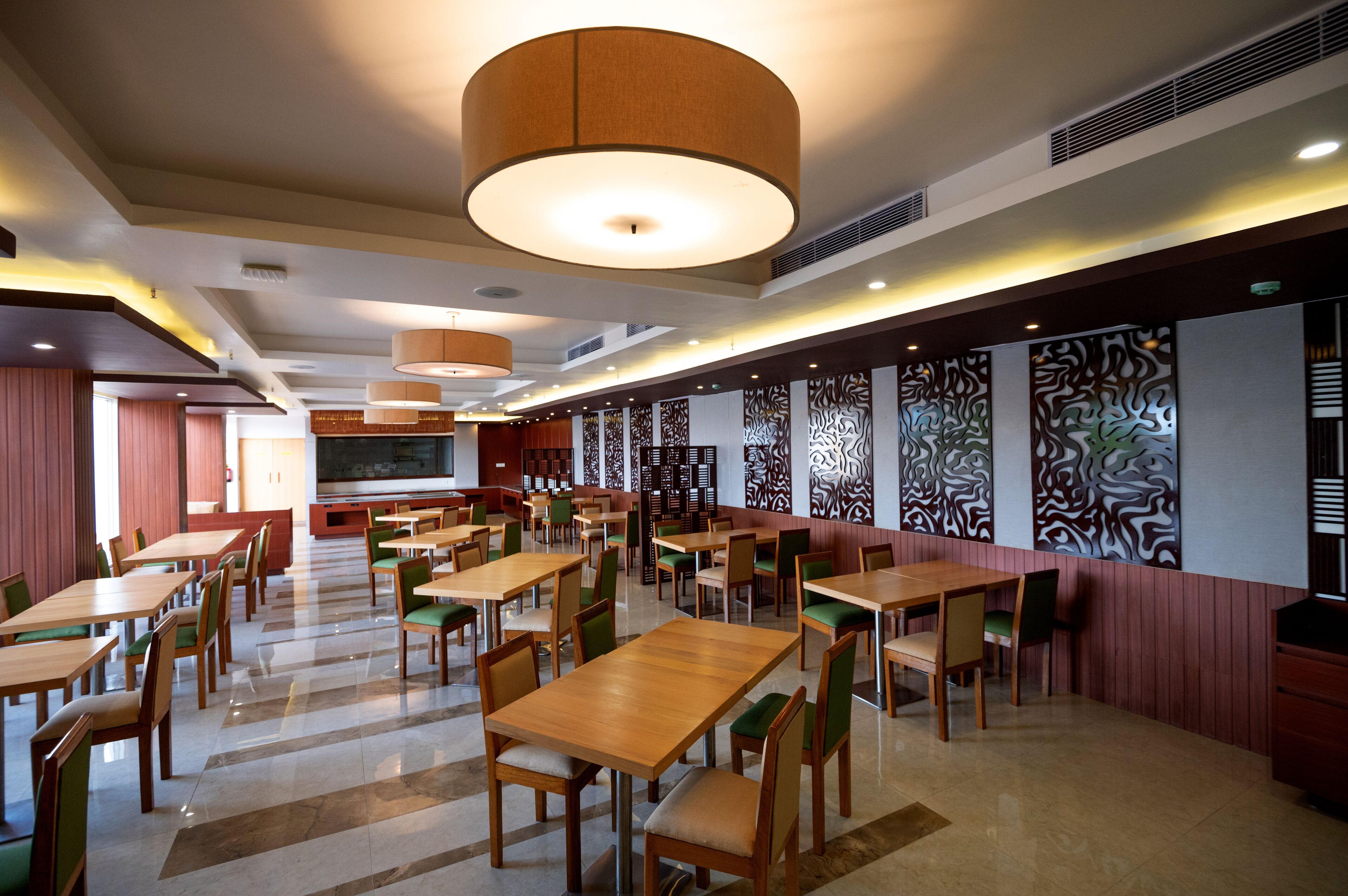 Um restaurante amplo com várias mesas e cadeiras, iluminação embutida e painéis decorativos nas paredes.