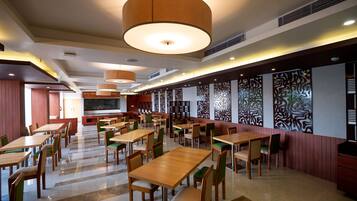 Um restaurante amplo com várias mesas e cadeiras, iluminação embutida e painéis decorativos nas paredes.
