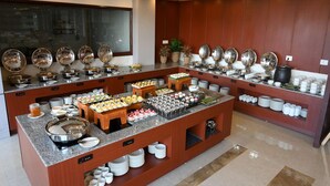A buffet setup with various food stations, including a fruit display, a dessert section, and a beverage area.