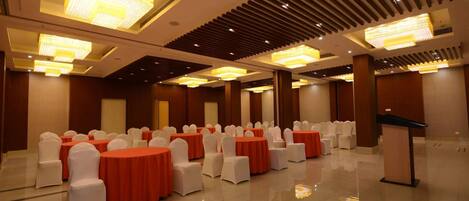 A banquet hall with rows of round tables, white chairs, and red tablecloths.