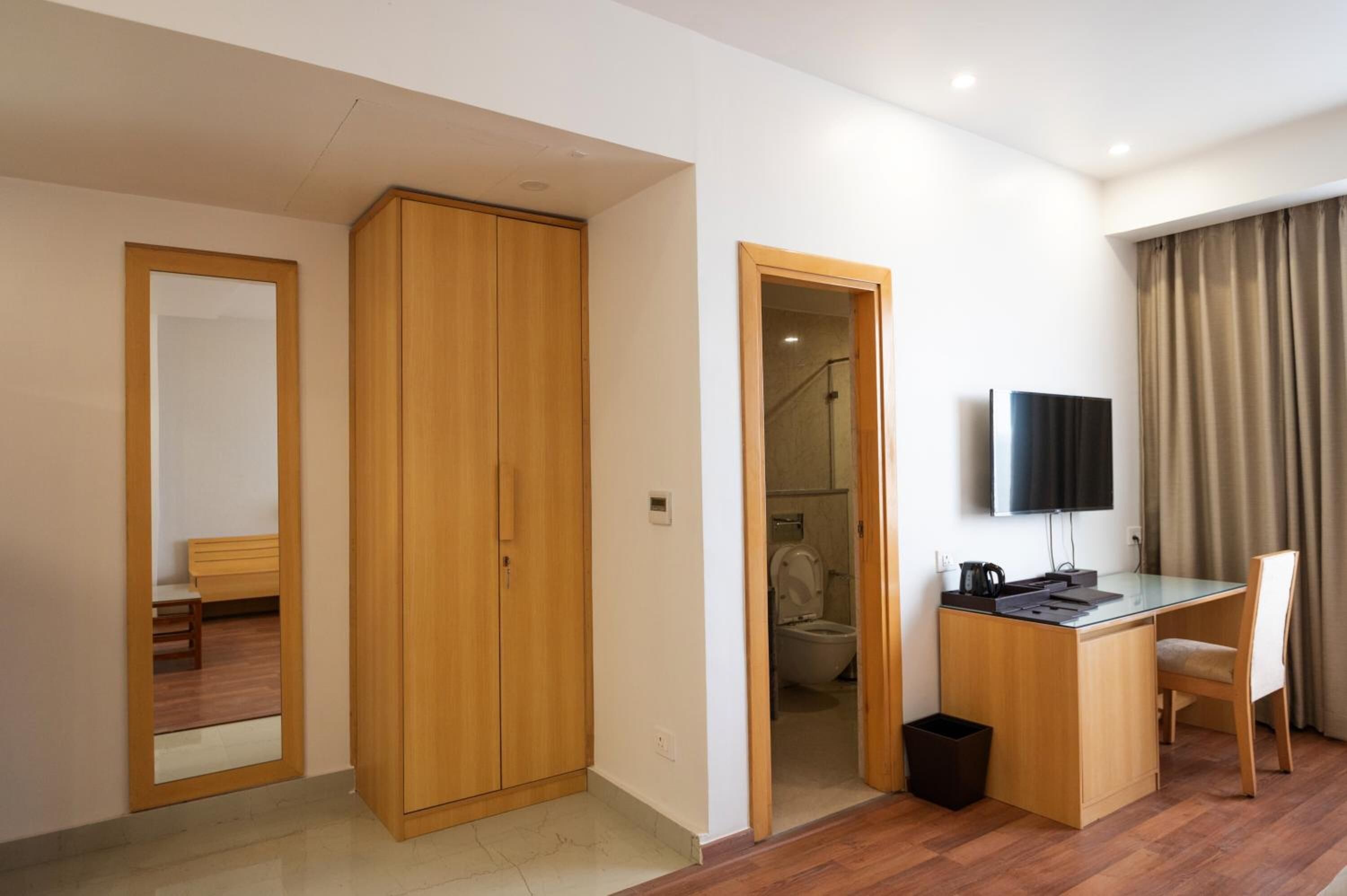 Habitación de hotel con un armario de madera, un escritorio con silla, televisión y un baño visible a través de una puerta abierta.