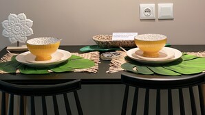 A dining area with a table set for two, featuring two wooden leaf-shaped wall decorations, a white flower sculpture, and two bowls on a woven placemat.
