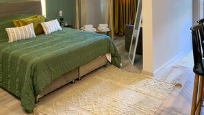 A modern bedroom with a large bed, a bedside table, a hanging light fixture, and a view of the bathroom.