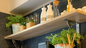 A kitchen shelf with potted plants, kitchenware, and a spice rack.