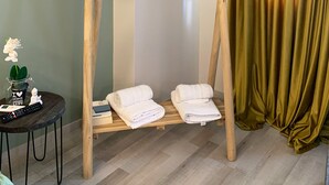 A room with a wooden towel rack, a small table with a remote control, and a green curtain.