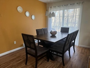 A dining area with a dark wooden table and chairs, a bowl on the table, and a window with curtains.