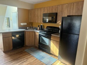 A kitchen with wooden cabinets, a black refrigerator, a stove, and a dishwasher.
