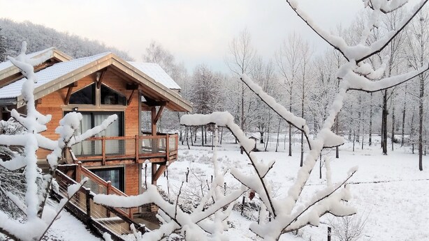 Une cabane en bois dotée d’un balcon, entourée d’arbres couverts de neige.