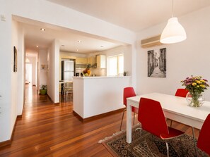 Cozinha moderna com armários brancos, uma ilha central e uma área de jantar com cadeiras vermelhas e uma mesa branca.