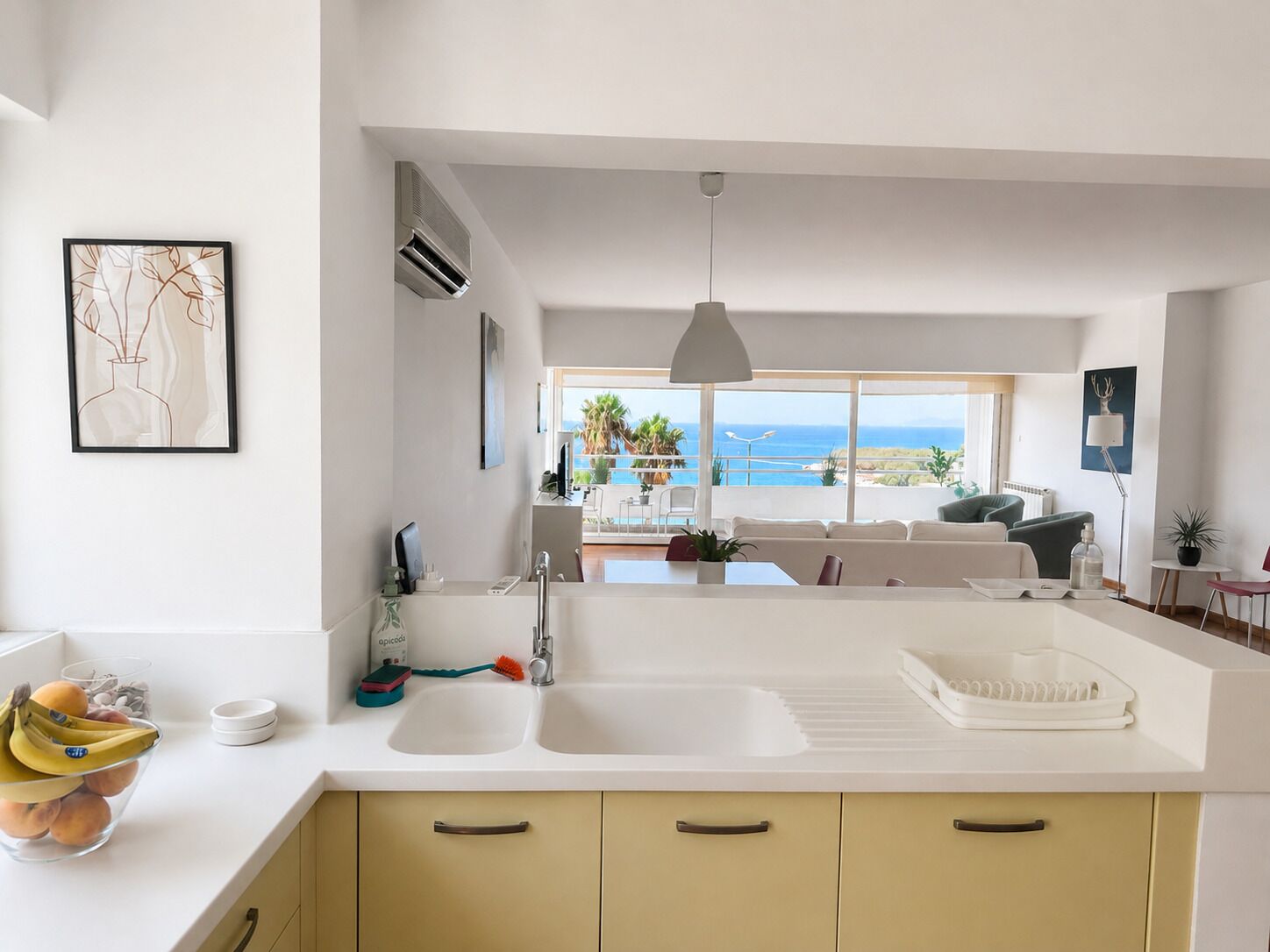 A modern kitchen with a large window overlooking a balcony, a dining area with a view, and a living space with a sofa and a table.