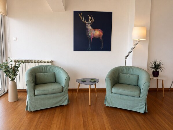 A room with two green armchairs, a small round table, a painting of a deer, a floor lamp, and a radiator. - Adelos Coastal Chic by the Sea - Athens Riviera (Alimos)