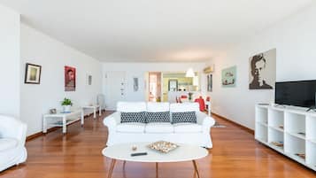 A modern living room with a white sofa, a coffee table, and a TV on a white stand.