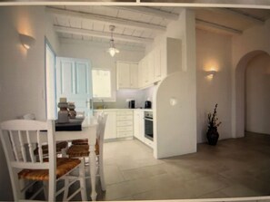 A modern kitchen with white cabinets, a dining area with white chairs, and a potted plant. - Magganari Moments 3 (Ios)