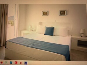 A hotel room with a bed, a nightstand, a lamp, and two wall-mounted picture frames. - Magganari Moments 3 (Ios)