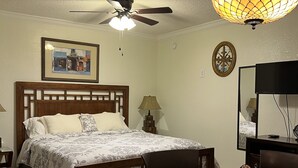 A bedroom with a bed, a desk, a chair, a ceiling fan, and a wall-mounted lamp.