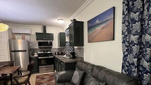 A modern kitchen with a refrigerator, oven, and microwave. There is a dining table with chairs and a sofa in the living area.
