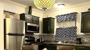 A modern kitchen with dark green cabinets, stainless steel appliances, and a wooden dining table with chairs.