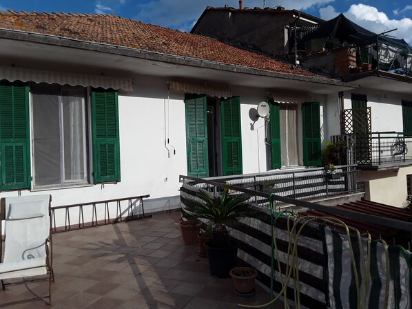 Un bâtiment aux murs blancs et aux volets verts, doté d’un toit en tuiles et d’un balcon avec une rambarde en métal.