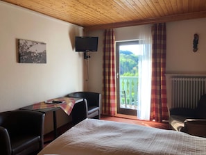 A hotel room with a bed, a desk with a chair, a television, and a balcony with curtains.