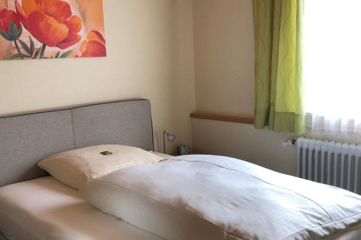 Een netjes opgemaakt bed met een grijs hoofdeinde, een wit kussen en een witte deken.