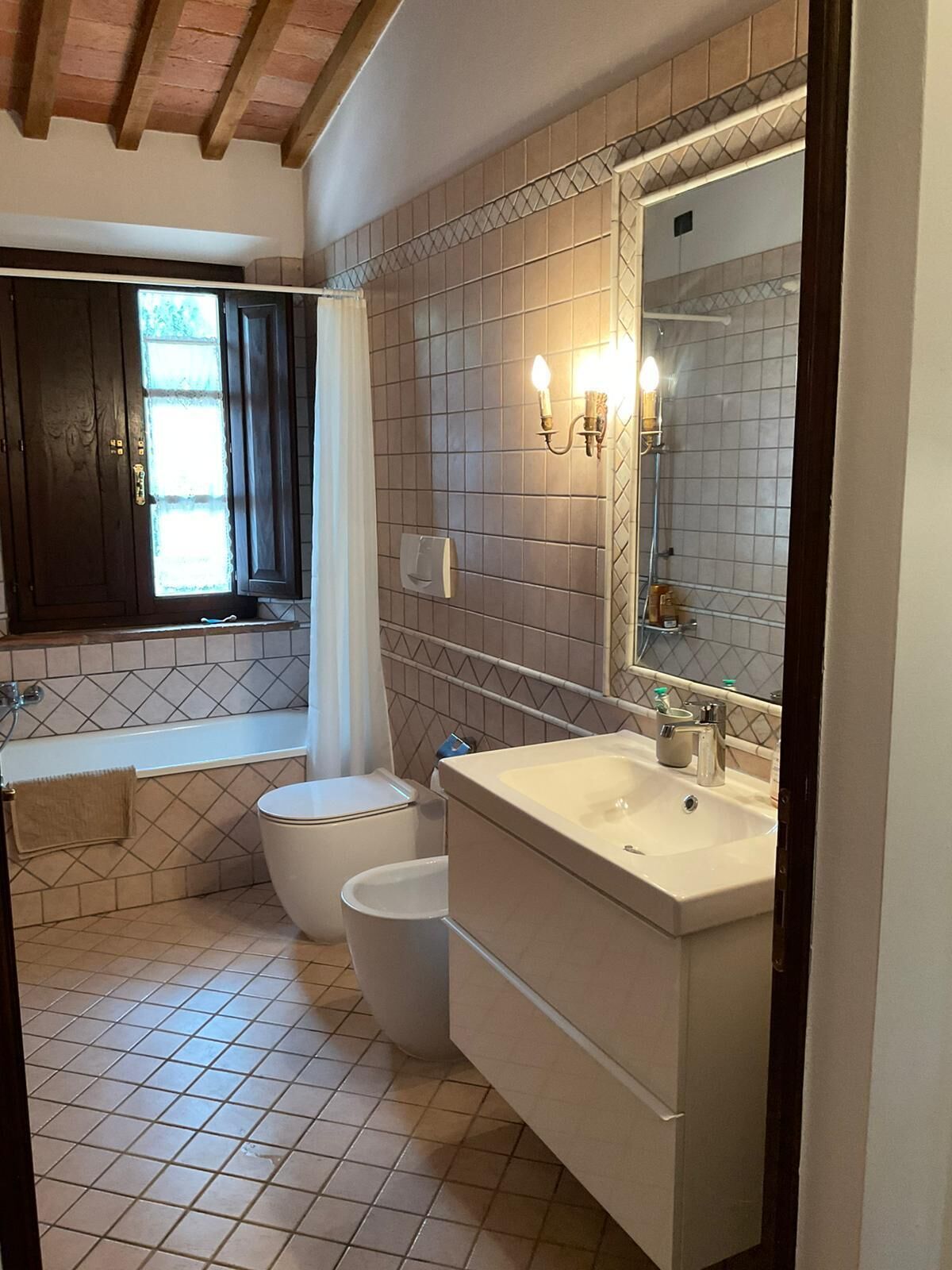Une salle de bain équipée d’une baignoire, de toilettes et d’un lavabo, avec des murs carrelés et un plafond en bois.