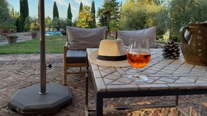 An outdoor seating area with a table, a glass of red wine, a straw hat, and a ceramic jug.