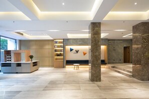 A modern lobby with a reception desk, seating area, and a staircase.