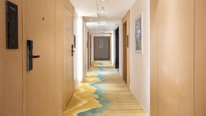 A hotel hallway with wooden doors, a carpet with a wave pattern, and a ceiling light fixture. - Ramada Encore by Wyndham Qingdao Shinan (Qingdao)
