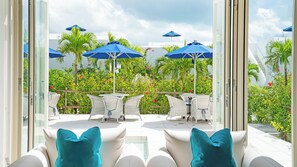 A balcony with white wicker chairs and blue cushions, overlooking a lush garden with red flowers and blue umbrellas. - Blue Ocean Hotel & Resort Miyakojima (Miyakojima)