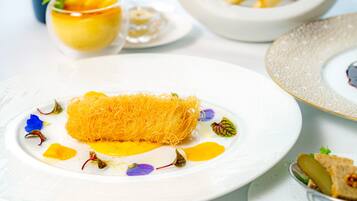 A plate with a dish featuring a golden, shredded texture, surrounded by colorful edible flowers and a yellow sauce.