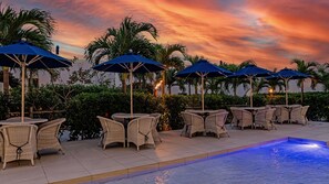 A poolside area with wicker tables and blue umbrellas, surrounded by palm trees and a sunset sky. - Blue Ocean Hotel & Resort Miyakojima (Miyakojima)