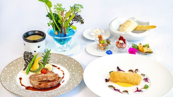 A variety of dishes on a table, including a steak with vegetables, a dessert with a golden roll, and several small plates with appetizers.