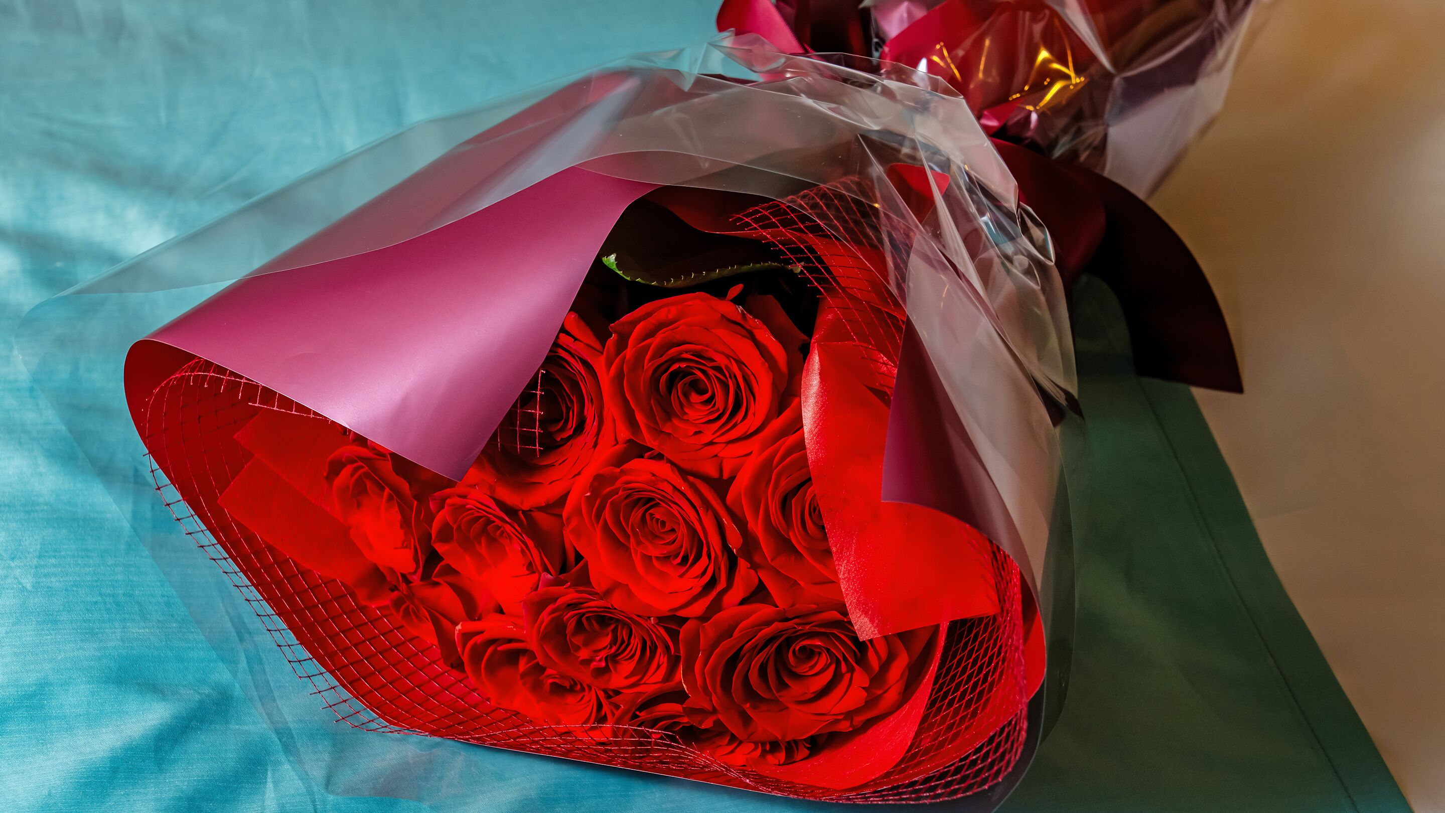 A bouquet of red roses wrapped in pink and clear paper, placed on a blue surface.