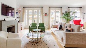 Een woonkamer met een open haard, groene stoelen, een ronde salontafel en een bank met meerdere kussens.