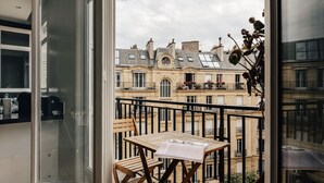 Een balkon met een houten tafel en stoelen, met uitzicht op een rij klassieke Europese gebouwen met meerdere ramen en balkons.